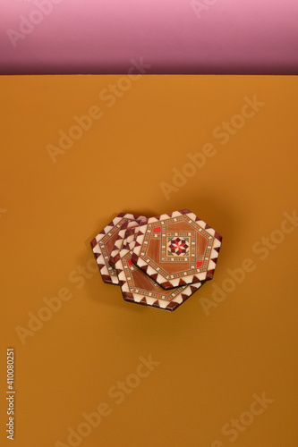 Vintage marquetery coasters with brown and beige colors. An eclectic oriental pattern made from mosaic wood on an ochre table and a pink background. Vertical shot