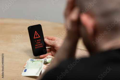Red warning text saying ‘I have your private pictures’ on a cell phone. A man, the sextortion victim holding his phone while being desperate. Cybercrime, ransomware