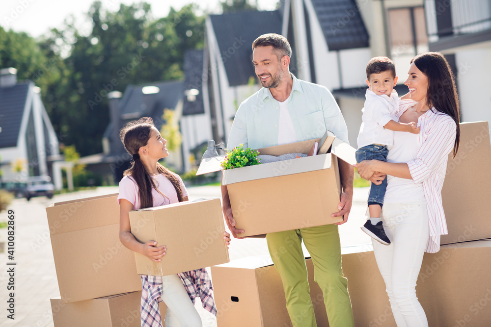 Portrait of four cheery people dad mom flat owners small little kids brother sister carrying boxes moving residence cottage Portrait of four cheery people dad mom flat owners small little kids brother sister carrying boxes moving residence cottage