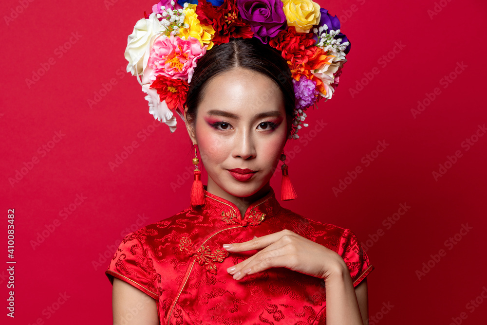 Fototapeta premium Gorgeous Asian woman in traditional Cheongsam dress with colorful make up and flower wreath on head in red isolated studio background