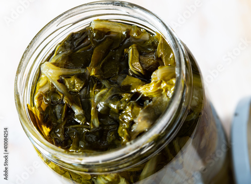 Closeup of open glass jar with pickled chard on wooden table..