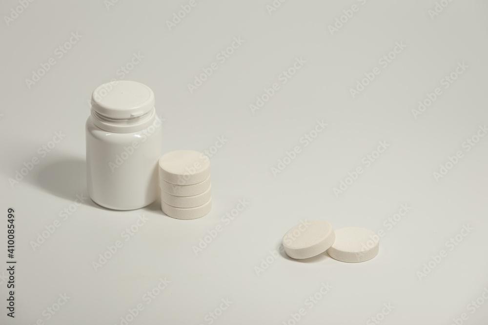 A round white pills and plastic container on the light background A round white pills and plastic container on the light background