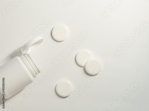 A round white pills and plastic container on the light background © Yurii Klymko