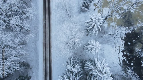 Beautiful aerial flight along snowy winter road with snow covered trees and icy river photo