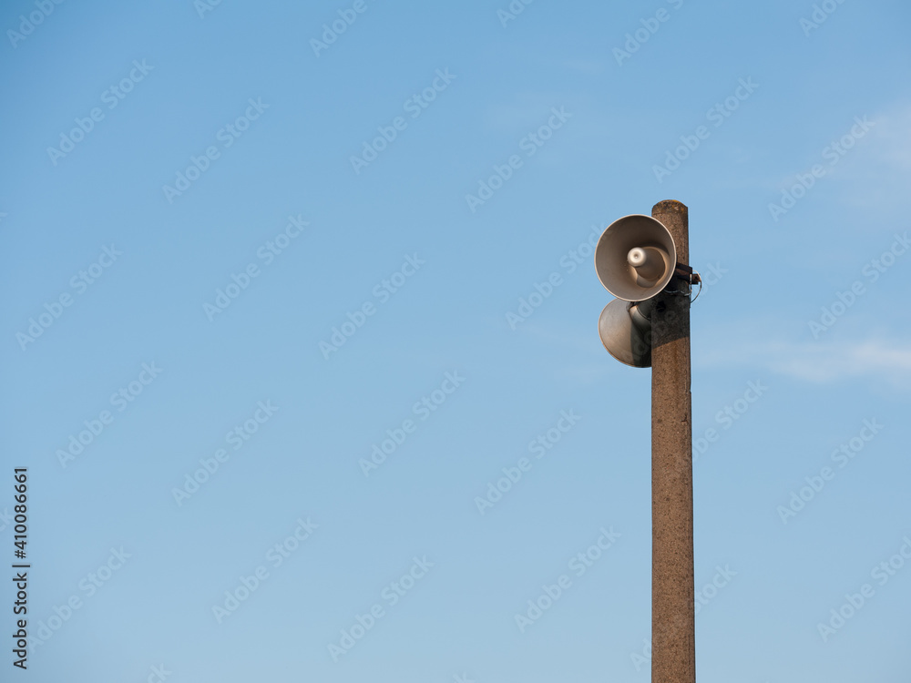 A cople of loudspeakers on the concrete pillar on the blue sky background. A cople of loudspeakers on the concrete pillar on the blue sky background.