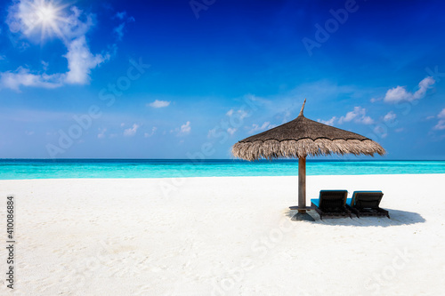 Fototapeta Naklejka Na Ścianę i Meble -  Two sunbeds under a parasol on a tropical paradise beach with blue sky, turquoise sea and copy space