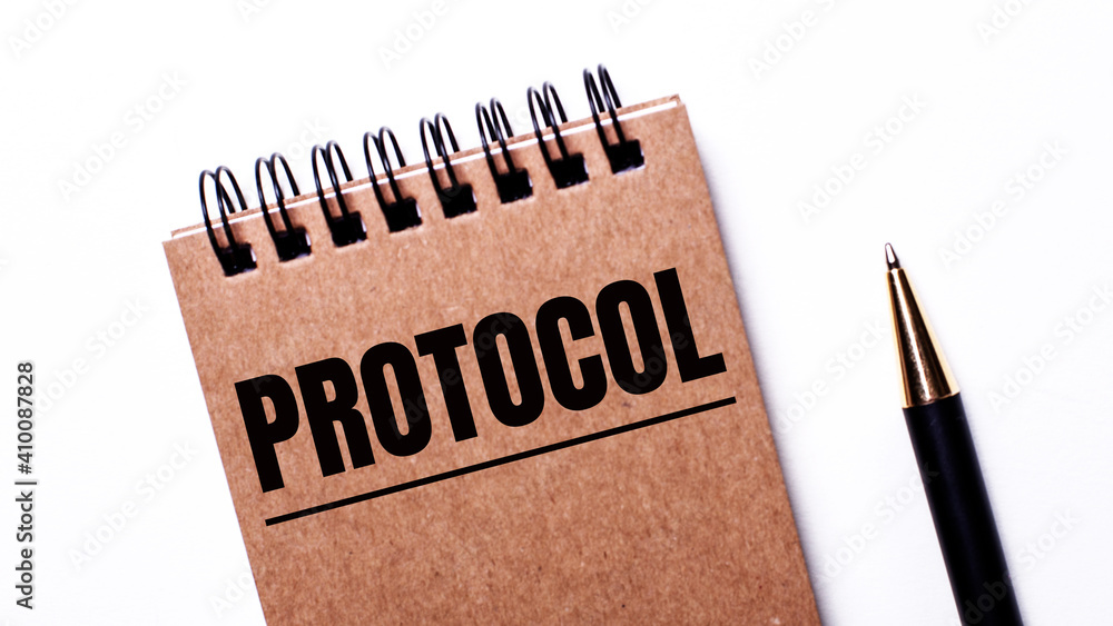 On a light background, a black pen and a brown notebook on black springs with the inscription PROTOCOL On a light background, a black pen and a brown notebook on black springs with the inscription PROTOCOL