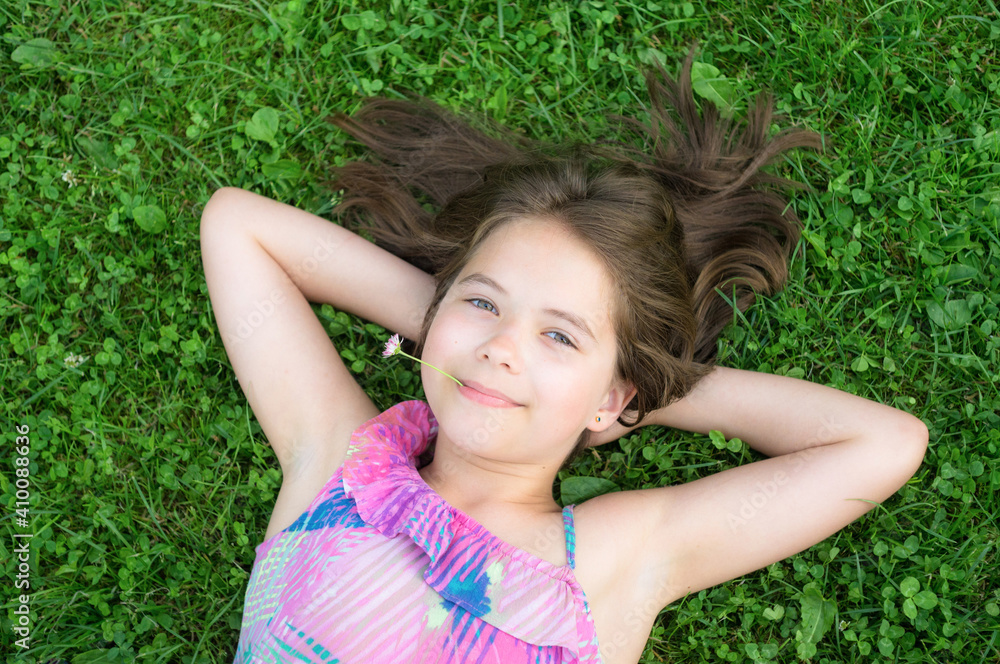 Young girl relaxing on a green clover meadow. Clover flower in the mouth. Portrait of a child. Young girl relaxing on a green clover meadow. Clover flower in the mouth. Portrait of a child.