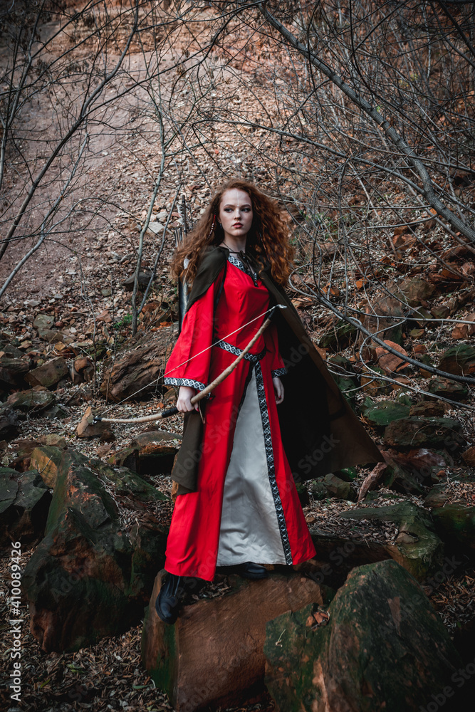 Red-haired woman in a red dress in a historical Celtic costume in the autumn forest Red-haired woman in a red dress in a historical Celtic costume in the autumn forest