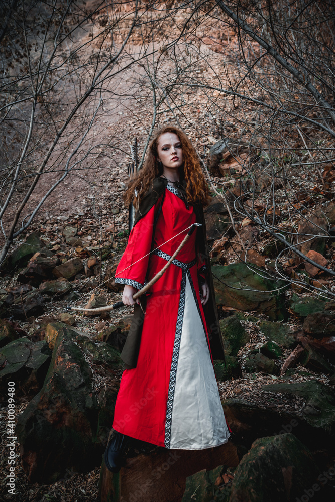 Red-haired woman in a red dress in a historical Celtic costume in the autumn forest