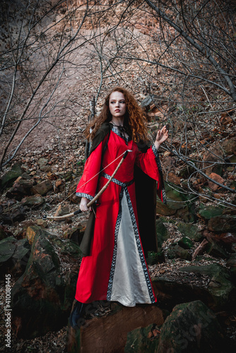 Red-haired woman in a red dress in a historical Celtic costume in the autumn forest