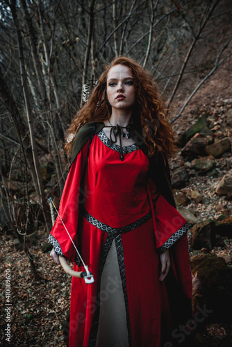 Red-haired woman in a red dress in a historical Celtic costume in the autumn forest