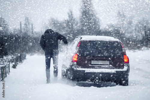 A man cleans a car from snow parked on the side of a winter road