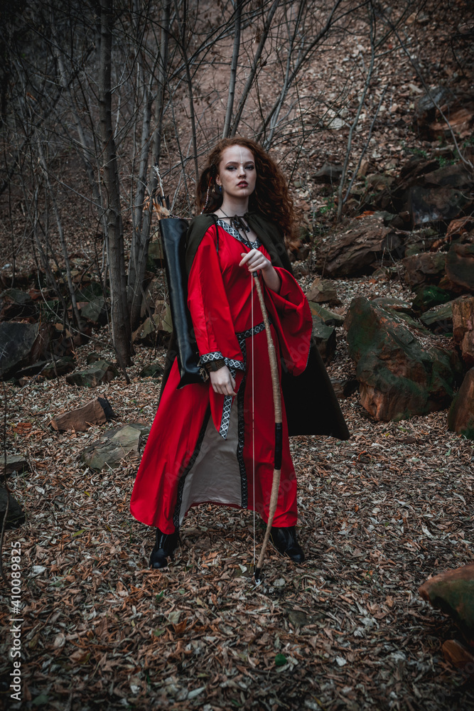 Red-haired woman in a red dress in a historical Celtic costume in the autumn forest Red-haired woman in a red dress in a historical Celtic costume in the autumn forest