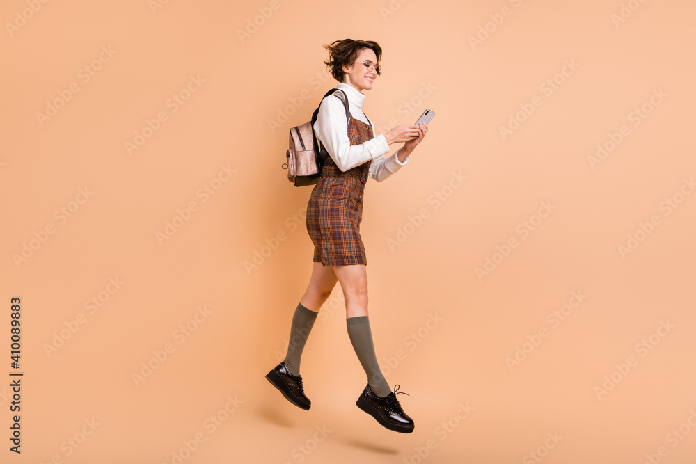 Full size profile photo of optimistic short hairdo girl jump run look telephone wear dress socks shoes isolated on peach background Full size profile photo of optimistic short hairdo girl jump run look telephone wear dress socks shoes isolated on peach background