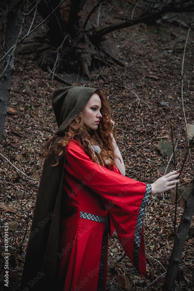 Red-haired woman in a red dress in a historical Celtic costume in the autumn forest Red-haired woman in a red dress in a historical Celtic costume in the autumn forest