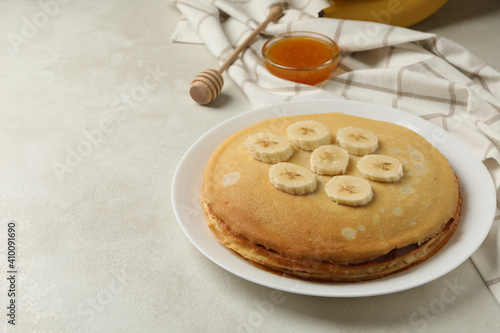 Concept of breakfast with plate of thin pancakes with banana, and jam on white textured background