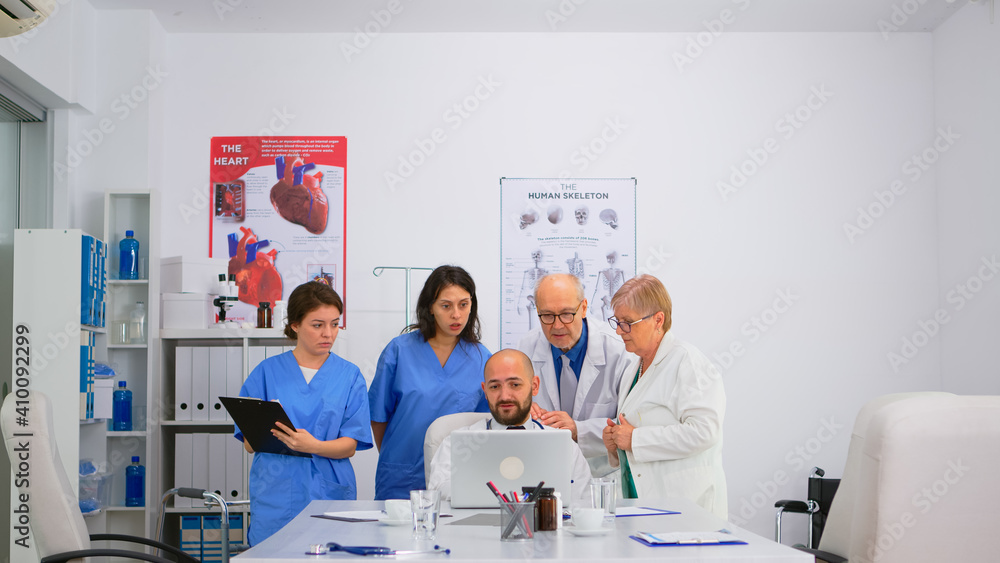 Obraz premium Doctors brainstorming examination of the symptoms patient at meeting room standing near specialist medic looking on computer. Profesional medical team working at hospital office making research