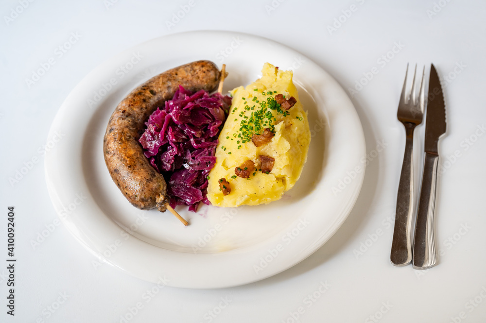 Baked bright pudding sausage with red cabbage and mashed potato on white plate.