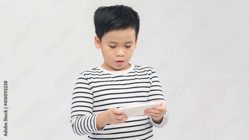 Portrait of an amused cute little kid playing games on smartphone isolated over white background