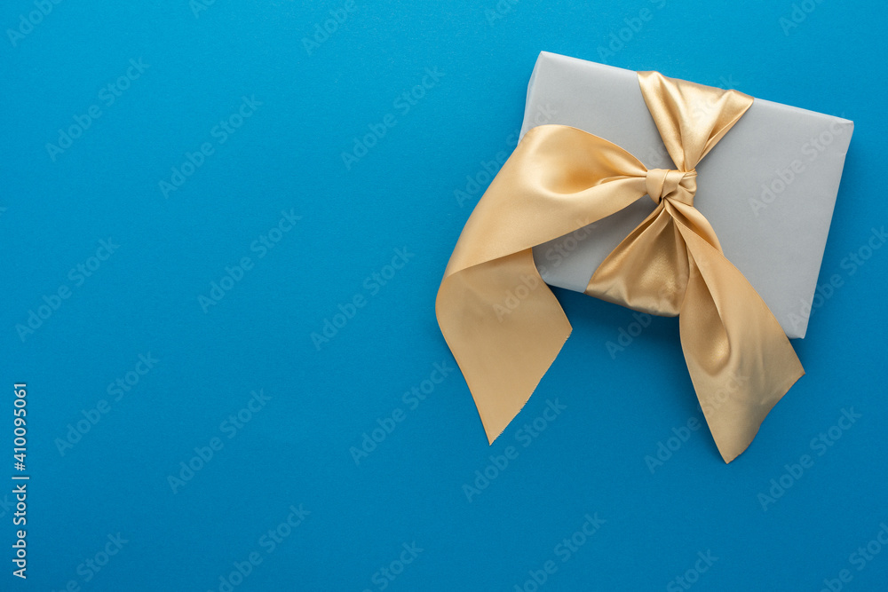 Gray gift box with golden bow on a blue background, birthday or valentine concept, top view, copy space