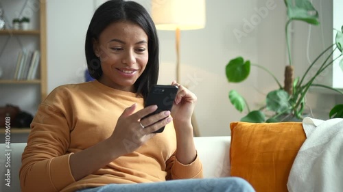 African woman saw surprise on phone on couch in house Spbd. Female model with black body skin sits in comfortable home and was pleasantly surprised by new on smartphone. Portrait of an attractive lady