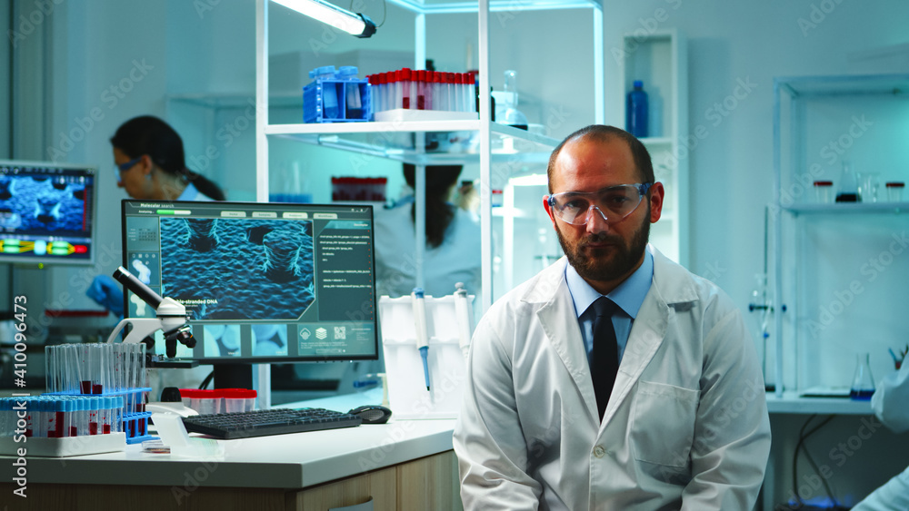 Tired doctor looking exhausted at camera in modern equipped lab late at night. Medical chemist team examining virus evolution using high tech and chemistry tools for research, vaccine development. Tired doctor looking exhausted at camera in modern equipped lab late at night. Medical chemist team examining virus evolution using high tech and chemistry tools for research, vaccine development.