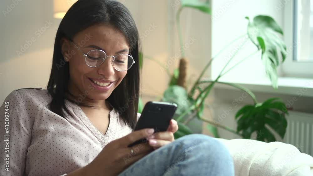 African woman in glasses with smile holds phone in hand background of window Spbd. Portrait of beautiful female model with black skin who is typing text on smartphone. Face of happy person in blouse African woman in glasses with smile holds phone in hand background of window Spbd. Portrait of beautiful female model with black skin who is typing text on smartphone. Face of happy person in blouse