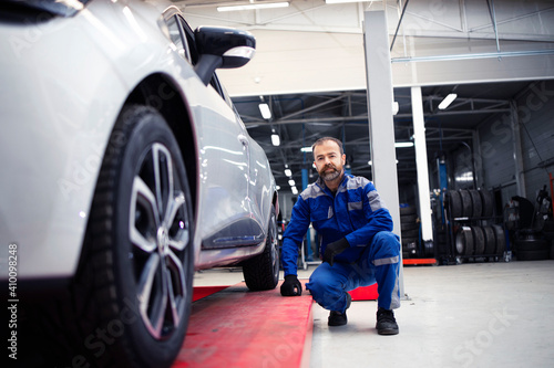 Portrait of professional car mechanic standing in vehicle workshop by an automobile.