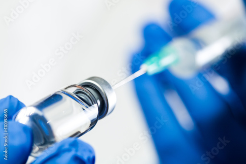 Obraz na plátně Hand in blue gloves holding syringe with needle inserted into ampoule with antiv