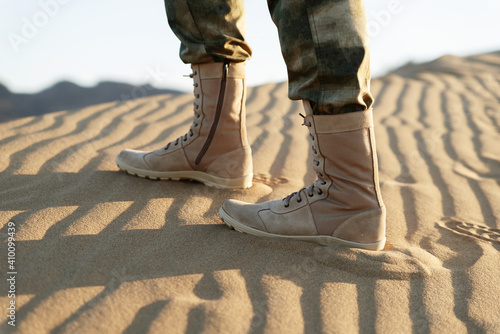 A man in army pants and zipper boots walks in the desert