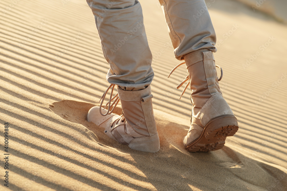 A man in beige clothes and boots walks through the desert