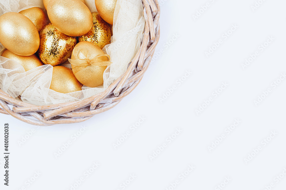 Top view of golden colored Easter eggs in wicker basket on white background. Happy Easter greeting card or wallpaper. Place for text. 