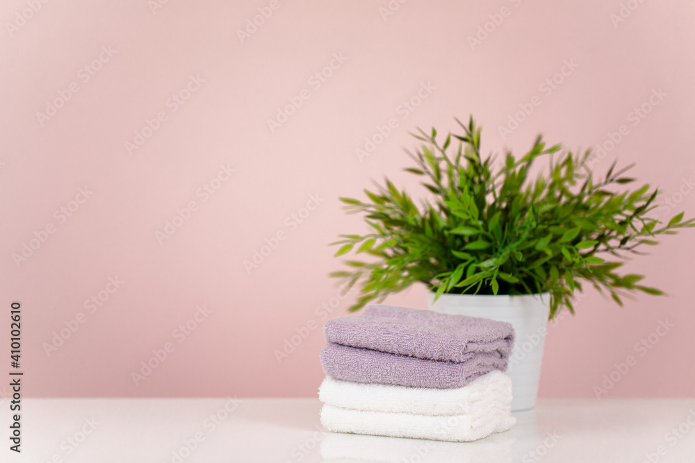 The concept of a spa salon. A stack of towels and a potted flower. Pink background. Copy space.