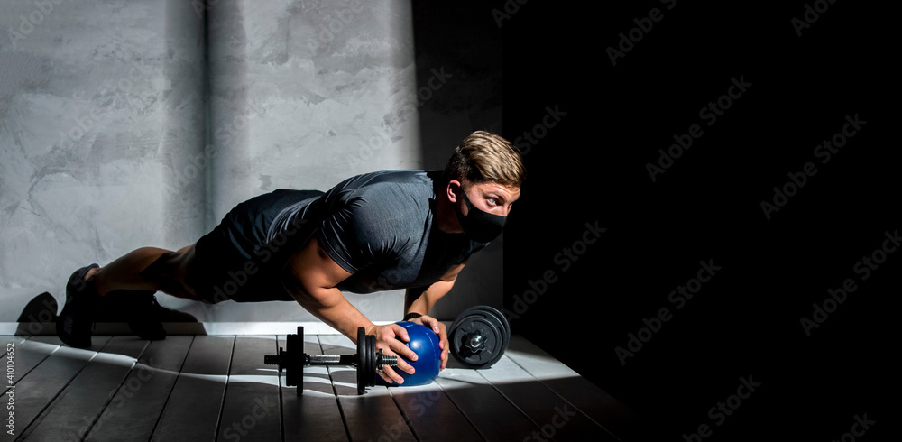 Fototapeta premium Male athlete wearing protective face mask and training with medicine ball in gym. Workout in gym after pandemic