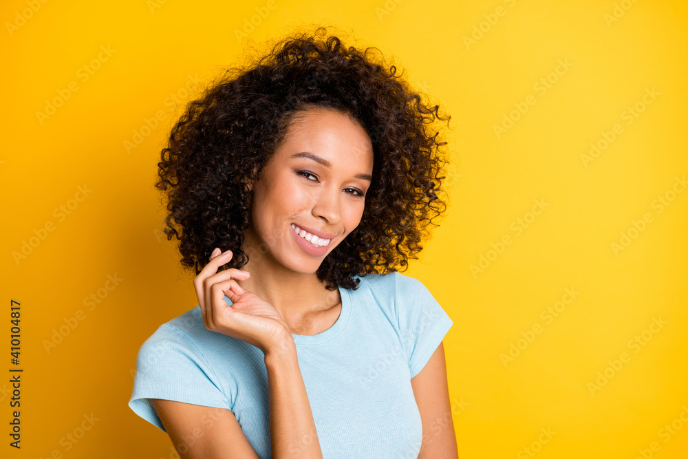 Photo of sweet adorable dark skin curly woman dressed blue t-shirt smiling hand arm hair isolated yellow color background Photo of sweet adorable dark skin curly woman dressed blue t-shirt smiling hand arm hair isolated yellow color background