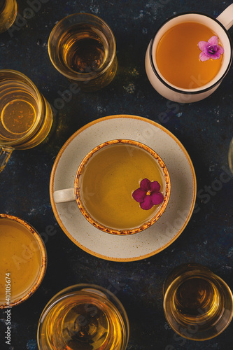 Many different cups of tea with violet flowers on dark blue background. Top view layout  photo