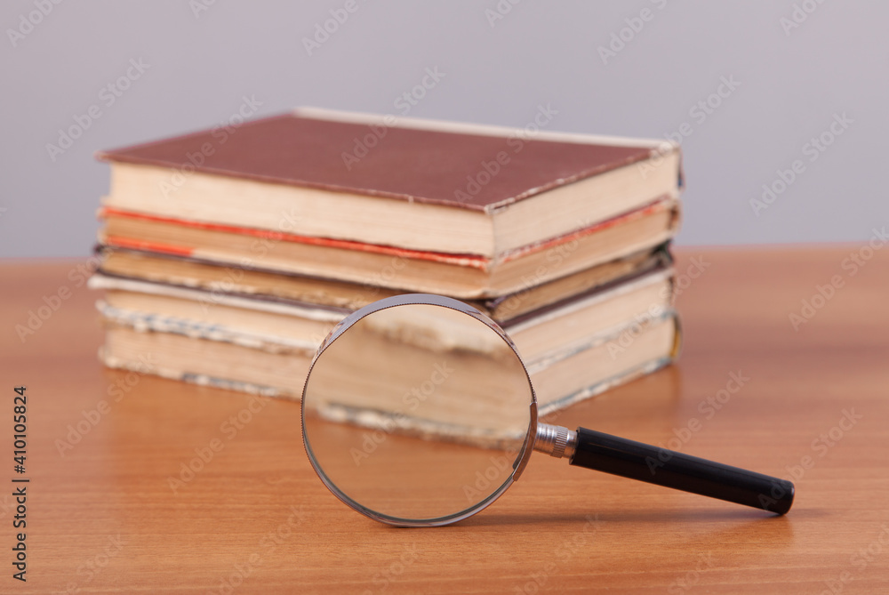 Books and magnifier an a wooden background. Black color magnifying glass. Books and magnifier an a wooden background. Black color magnifying glass.