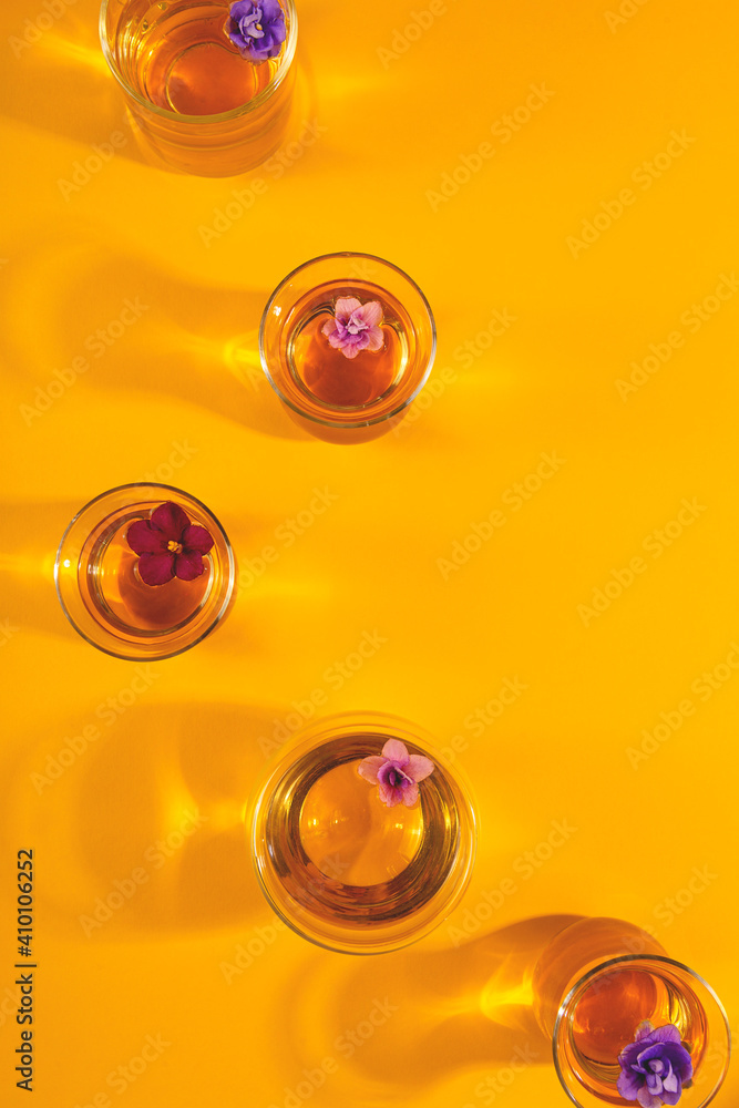 Many different transparent cups of tea with flowers on a yellow background. Copy space