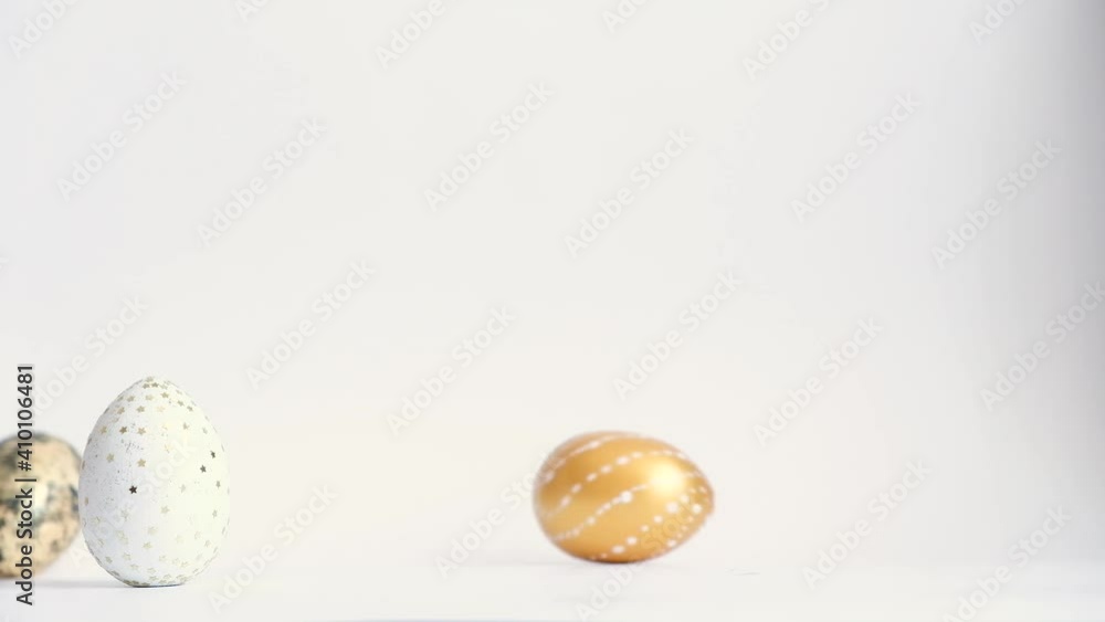 Egg are rolling on the white table, knock each other. Easter golden decorated eggs isolated on white background. Minimal easter concept. Happy Easter card Egg are rolling on the white table, knock each other. Easter golden decorated eggs isolated on white background. Minimal easter concept. Happy Easter card