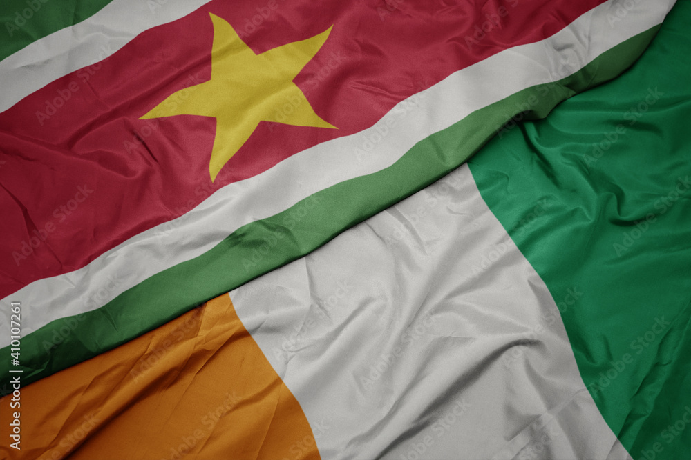 waving colorful flag of cote divoire and national flag of suriname.