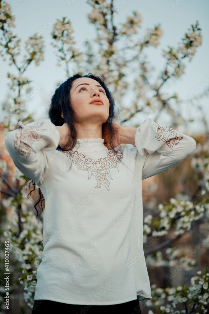 Nice looking girl holding from her neck and looking at the sky in spring, during cherry blossom