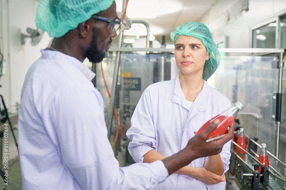 Obraz premium Caucasia worker Factory girl look at African man for discussion with product in bevrage industry