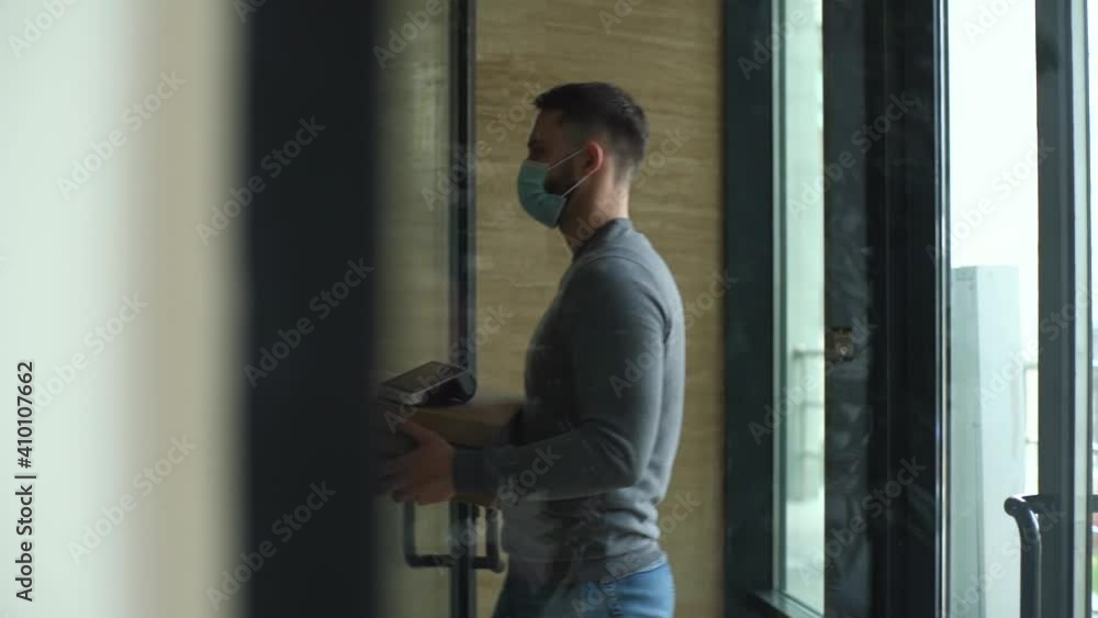 Courier with boxes hot pizza and payment terminal enters lobby of an apartment building. Delivery man in medical mask walks into lobby of office building to meet customer and hand over online order. Courier with boxes hot pizza and payment terminal enters lobby of an apartment building. Delivery man in medical mask walks into lobby of office building to meet customer and hand over online order.