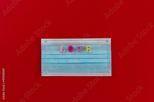 Blue medical mask with wooden multicolored letters with the inscription "LOVE" on red background. The concept of Valentine's Day and coronavirus. Theme of love banner. Loving, positive emotions