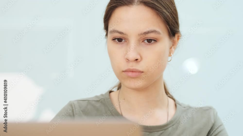 A serious woman is working using laptop computer while holding a pencil sitting in the office A serious woman is working using laptop computer while holding a pencil sitting in the office