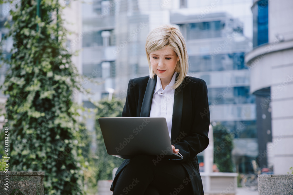 Young woman working on a laptop outdoors in a business hub neighborhood. Young woman working on a laptop outdoors in a business hub neighborhood.
