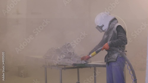 The man is sandblasting the detail. Sandblast metal parts. Sandblasting gun photo