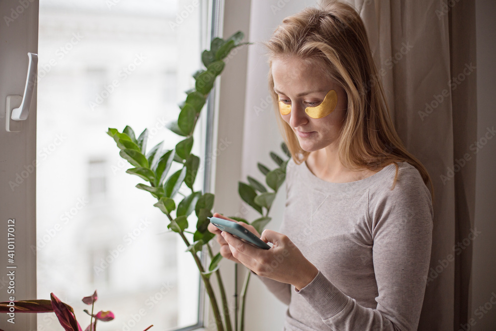 A young woman is shopping online, standing by the window and holding a mobile phone and a credit card. The concept of modern shopping A young woman is shopping online, standing by the window and holding a mobile phone and a credit card. The concept of modern shopping