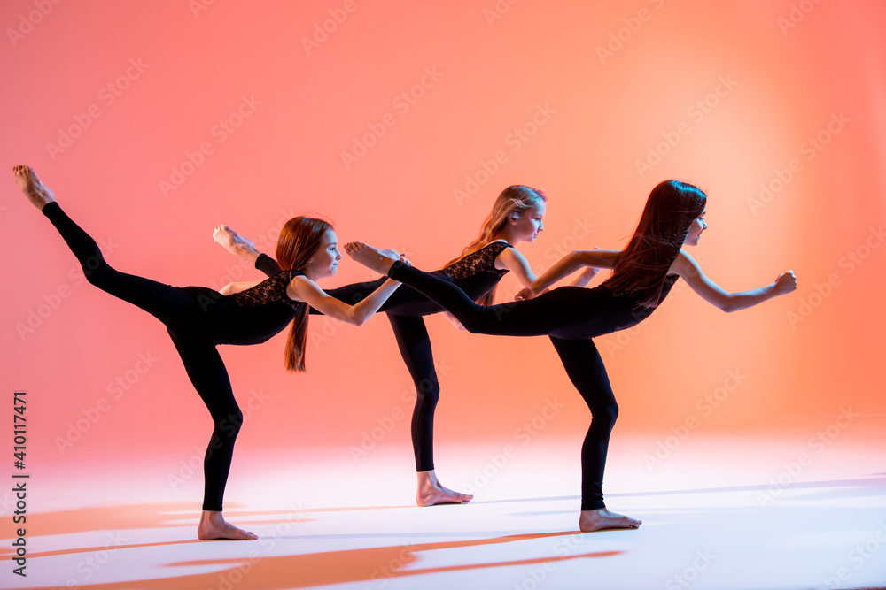 group of three ballet girls in black tight-fitting suits dancing on red background with their long hair down.
